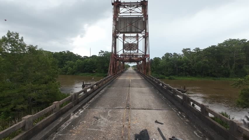 A footage on a rusty camelback truss bridge spans a quiet road through forest, part of historic Route 66 in Missouri
