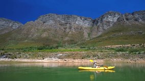 A person rowing a yellow canoe from left to right across calm turquoise waters, surrounded by dramatic mountains in South Africa’s wine region. The still pond reflects the peaks and blue sky. - Powered by Shutterstock - Get 15% off with code: PIKWIZARD15