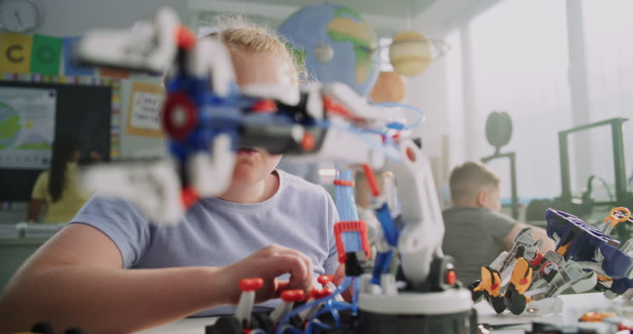 Elementary School Girl Sitting at the Desk, Studying Model of Innovative Robotic Arm. Teacher Helping Smart Young Student. Science, Engineering and Advanced Technology Lesson. Interactive STEM Class.