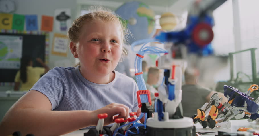 Elementary School Girl Sitting at the Desk, Studying Model of Innovative Robotic Arm. Teacher Helping Smart Young Student. Science, Engineering and Advanced Technology Lesson. Interactive STEM Class.