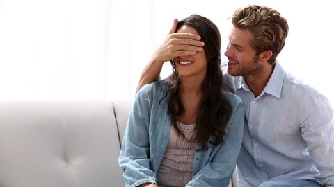 Man surprising his partner with engagement ring at home on the couch