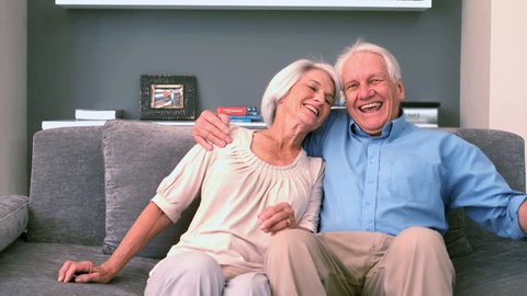 Retired Caucasian couple sitting down on the couch and smiling in slow motion