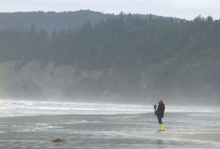 Woman at Haystack Rock in Cannon Beach, Oregon wearing yellow boots walks the
