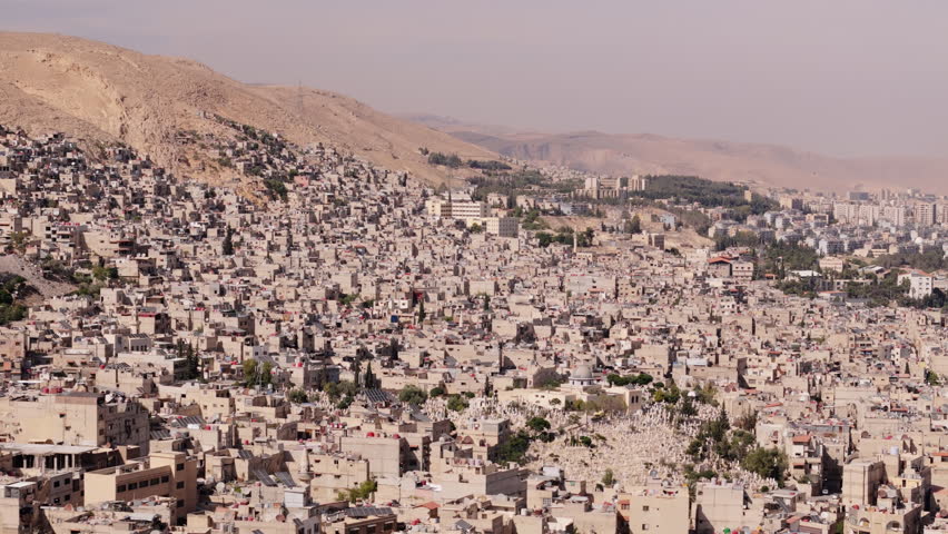 Drone slides sideways over Damascus, Syria during daytime, revealing the city’s architecture, streets, and urban layout from above.