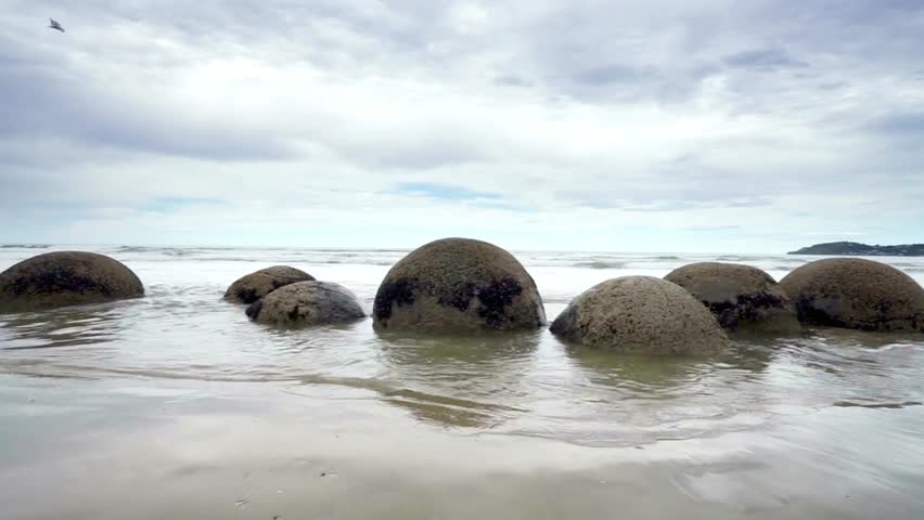 Moeraki boulders on koekohe beach in new zealand on a cloudy day with ocean waves