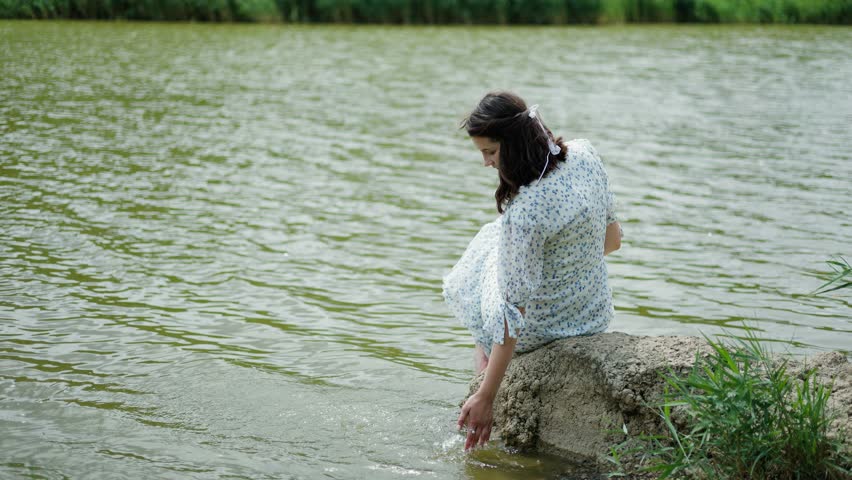 A girl enjoys the beautiful and peaceful atmosphere of nature on the edge of a lake.