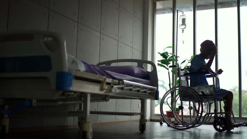 Depressed patient woman with cancer sitting on wheelchair suffering headache
and looking out the window after chemotherapy at hospital, sickness female
wearing head scarf feeling unwell and lonely.