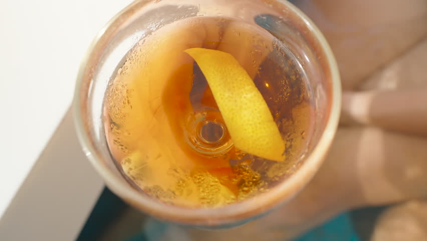 Top down view inside cocktail glass showing lemon peel floating in amber liquid, held by person over pool, Artistic Beverage Concept.
