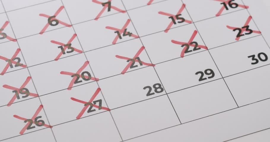 Close-up of a calendar being marked with a red marker showing crossed-out dates indicating passage of time, planning, tracking, and time management.