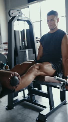 Focused man exercising with a leg extension machine in a gym, working on lower body strength and fitness. Man Working Out at Gym Using Leg Extension Machine for Strength Training Vertical
