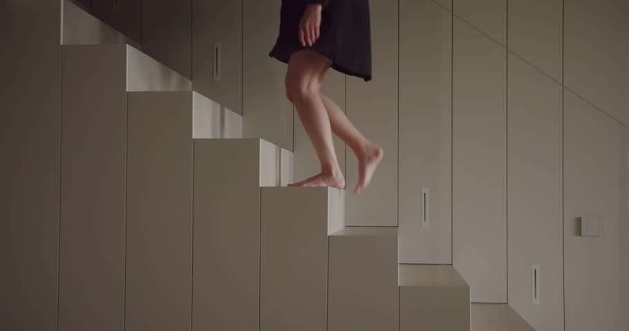 A woman stands barefoot atop geometric, cuboid structures within a monochrome, minimalist room, creating a serene and artistic scene. Woman Balancing on Cuboid Structures in a Minimalist Room