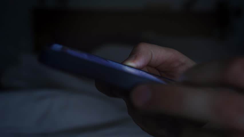 Smartphone and social network addiction concept. Hands using smartphone in bed at night
