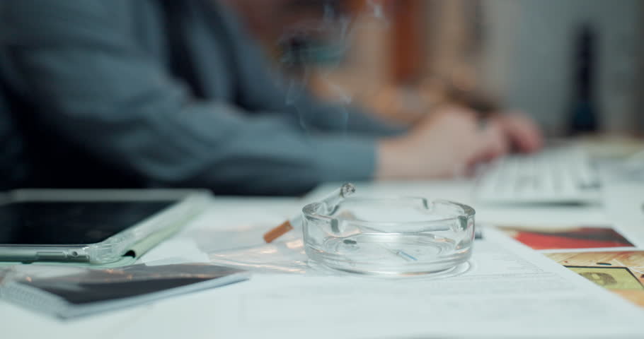 Officer, hands and smoking with cigarette on desk for private investigation, stress or nicotine. Person, detective or smoker with ash tray at night for crime scene research, evidence or serial killer