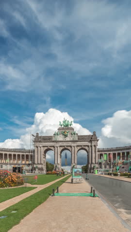 Hyperlapse of the Cinquantenaire Arcade in Jubelpark with flowerbed, Brussels, Belgium. The memorial triumphal arch stands tall under clouds timelapse, symbolizing Belgian history and independence.