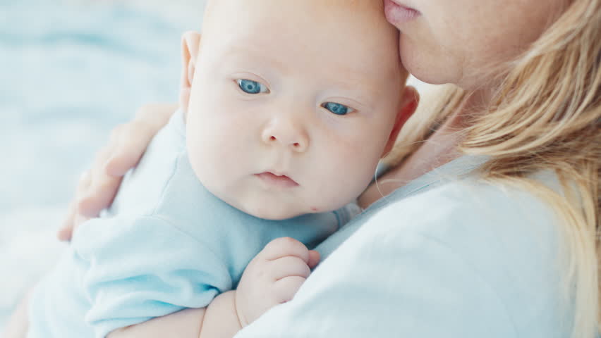 Mother caresses her newborn son with deep blue eyes in a bright room