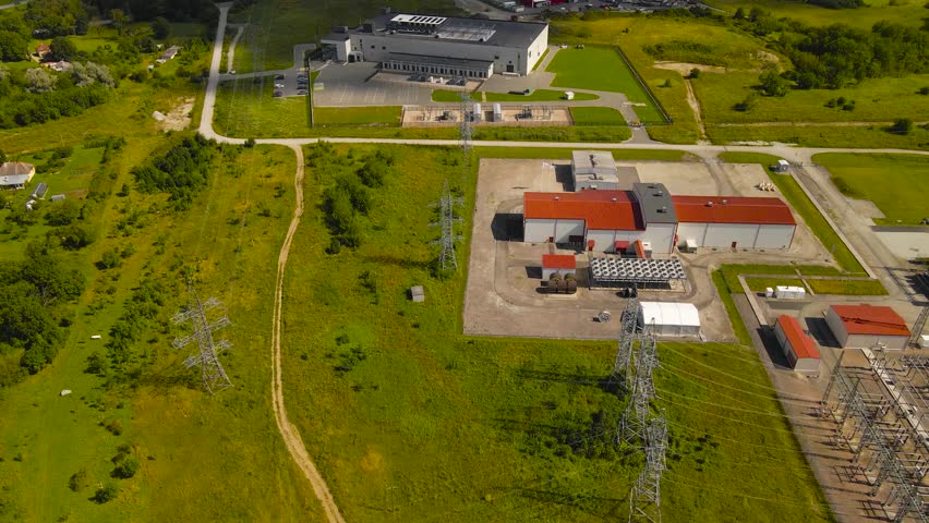 Aerial drone revealing shot of a large electrical power distribution substation and a modern server data center in the background during summer sunny day at Baltics countryside. Power lines visible.