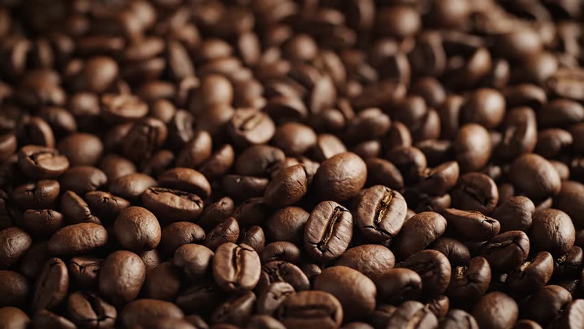 Macro, slow-motion shot of roasted coffee beans being stirred or falling. Detailed texture and rich brown colors.