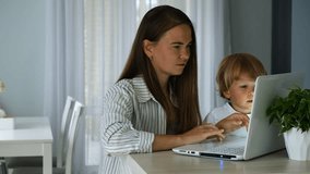 Mom and laptop for work from home with child sitting next to her. Parent balancing work and childcare. Working on a laptop set up in a kitchen table in living-room. Online job business work. - Powered by Shutterstock - Get 15% off with code: PIKWIZARD15