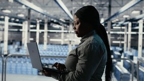 IT expert monitors server farm activity using laptop while walking in facility. African american woman in data center reviews rigs tests results to ensure systems are working correctly, camera B - Powered by Shutterstock - Get 15% off with code: PIKWIZARD15