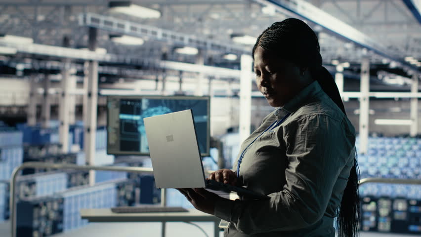 Data center admin monitors deep learning process with laptop, reviewing operational metrics. African american woman using device to review neural networks reports during inspection, camera B - Powered by Shutterstock - Get 15% off with code: PIKWIZARD15