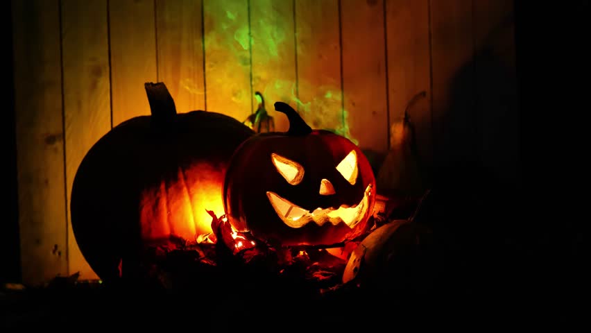 Jack o lantern background. Halloween spooky background. Evil glowing pumpkin with green smoke in autumn leaves on wooden background. 4k footage