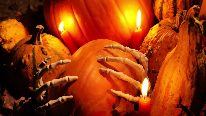 Halloween pumpkins background. Pumpkin in skeletal hands by candlelight. Pumpkins set, bone hands and red candles in the dark. 4k footage