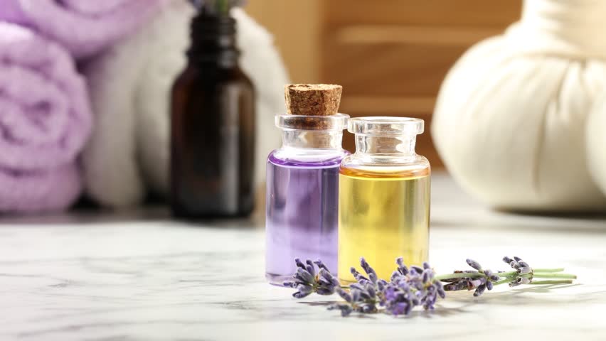 Dripping lavender essential oil into bottle at white marble table, closeup. Space for text