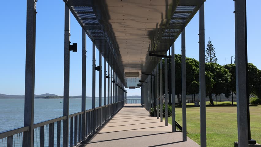 Covered walkway supported by metal columns with the ocean and trees at East Shores in Gladstone, Queensland, Australia