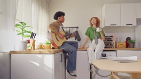 Diverse young adult couple spend quality time together in house. Attractive man and woman friend playing guitar and socializing in cozy kitchen, enjoy each other's company in warm and relax atmosphere - Powered by Shutterstock - Get 15% off with code: PIKWIZARD15