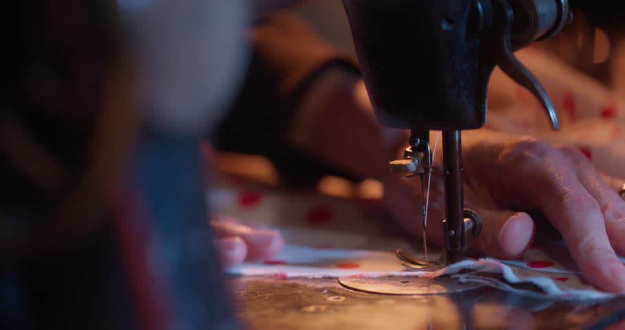 Close-up shots of vintage sewing machines in use, fabric being stitched, threaded and adjusted by hand under soft cinematic lighting. Some clips include slow motion and detailed mechanisms.