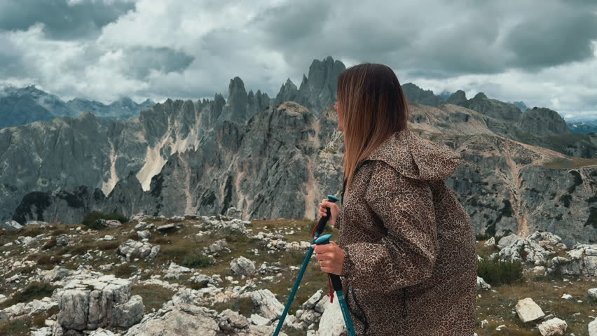 Female hiker walking in the mountains holding hiking poles and admiring the Tre Cime di Lavaredo, Dolomites, Italy