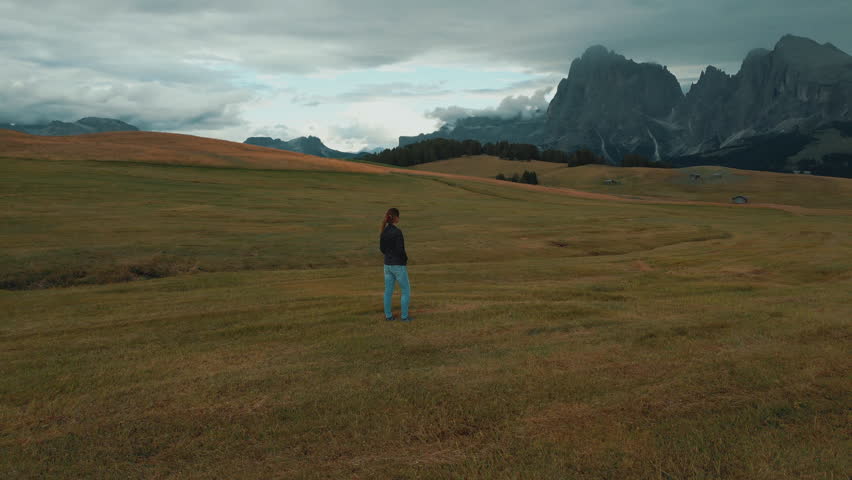 Woman standing in a field admiring the majestic peaks of the Dolomites in Alpe di Siusi, Italy