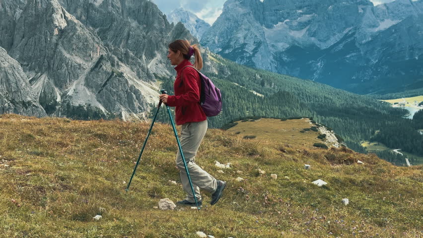 Female hiker walking along mountain trail, featuring iconic Cadini di Misurina rising dramatically against summer sky in scenic Dolomites landscape