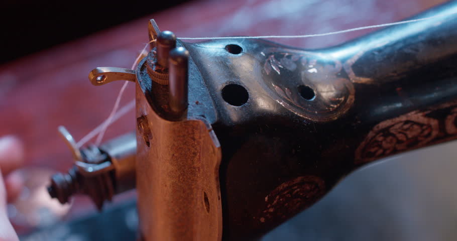 Close-up shots of vintage sewing machines in use, fabric being stitched, threaded and adjusted by hand under soft cinematic lighting. Some clips include slow motion and detailed mechanisms.