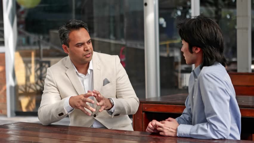 Diverse international business professionals collaborating during strategic meeting at urban Melbourne cafe, gesturing while discussing potential partnership