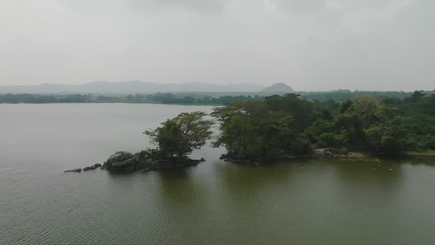 An aerial view showcasing the peaceful lakeside greenery of Sri Lanka, with calm waters and lush forested shores.