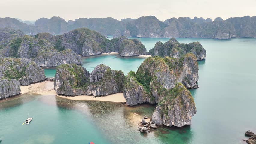 Rugged limestone islets rise above turquoise waters with sandy coves in the UNESCO-listed Ha Long Bay, Quang Ninh Province, Vietnam, captured by aerial drone shot.