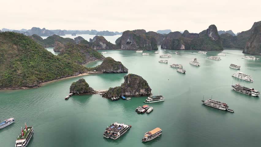 Smooth aerial glide above Ha Long Bay, Vietnam, showcasing emerald waters, limestone karst islands, and numerous tourist cruise boats scattered across the bay.