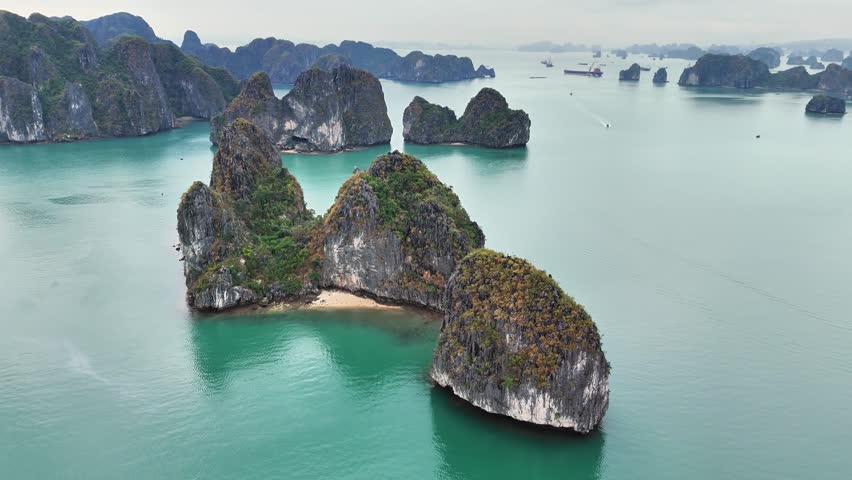 Rugged limestone karsts enclose a small sandy beach in the turquoise waters of UNESCO-listed Ha Long Bay, Quang Ninh Province, Vietnam, captured by aerial drone orbiting shot.