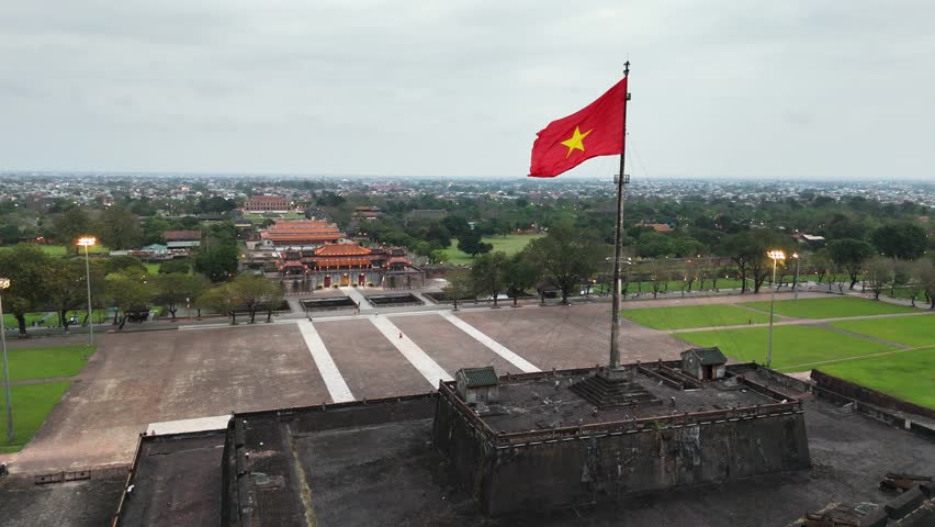 Large Vietnamese flag atop the flag tower of Hue Citadel, facing the Ngo Mon Gate and Imperial City beyond, central Vietnam, captured by dolly-in drone shot.