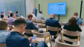 Business professionals attending a presentation, engaging with their devices, modern conference setting. - Powered by Shutterstock - Get 15% off with code: PIKWIZARD15