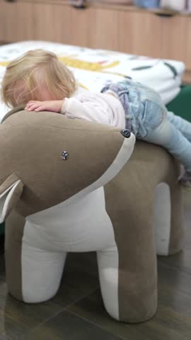 Bblonde toddler transitions from peaceful slumber on a plush deer ottoman to playful exploration in cozy room, highlighting charming animal-themed furniture