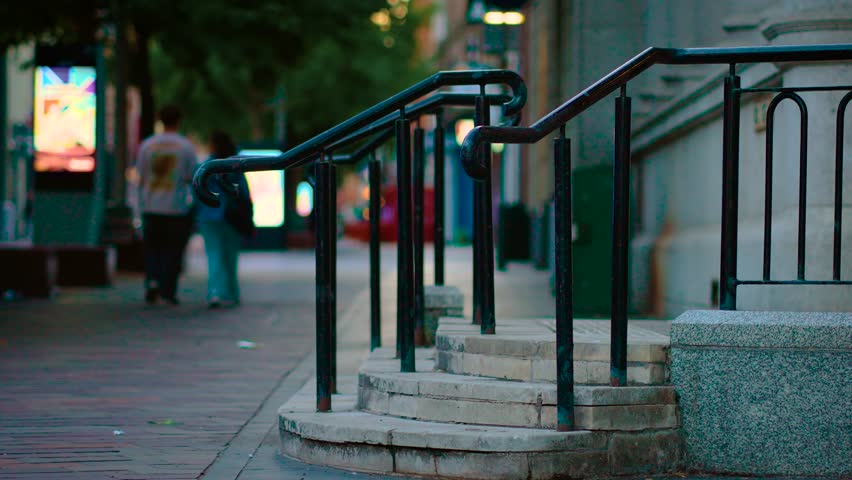 Stairs curving gently upward with metal railings on quiet evening street. Steps leading toward building entrance while pedestrians passing by. Stone staircase standing still beside sidewalk under city
