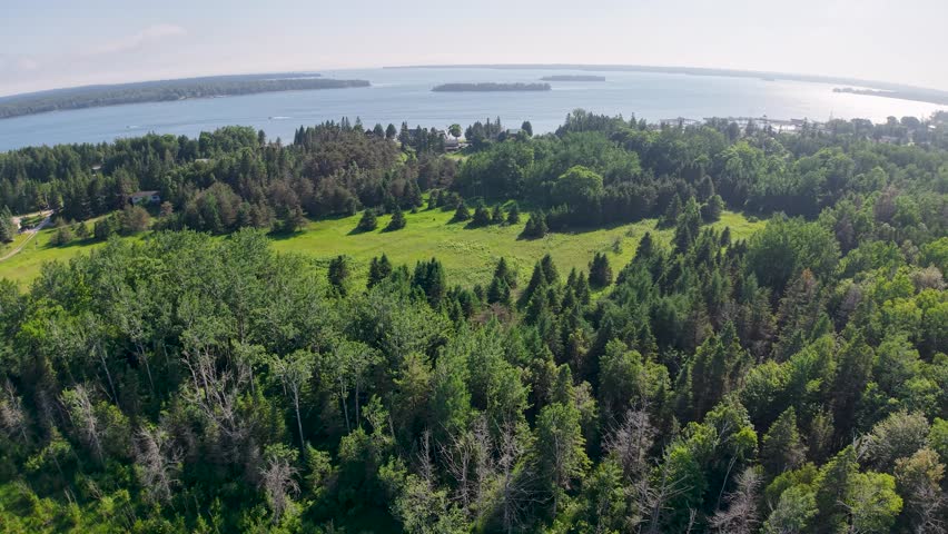 Aerial drone view of lush green forest and open meadow along a scenic lakeshore in Michigan’s Upper Peninsula.