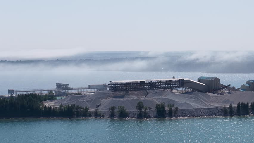 Aerial drone view of an industrial quarry facility along the Lake Huron shoreline in Michigan’s Upper Peninsula with mist over the water.