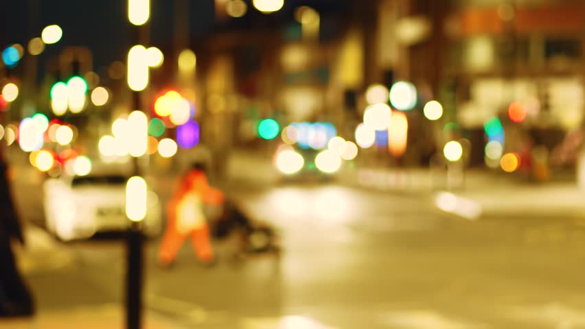 Blurred pedestrians dangerously crossing street in front of approaching car. Out of focus figures running through traffic under glowing lights. Defocused people dashing across urban road with