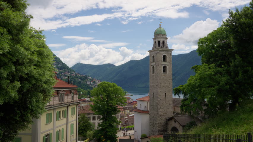 A scenic view of an old church overlooking the city of Lugano, Switzerland, with the Swiss Alps rising majestically in the background.