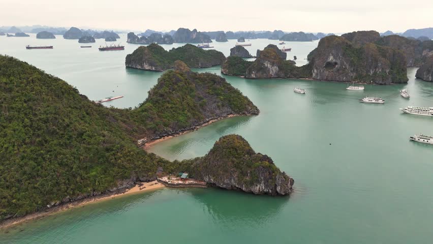 Aerial view over Ha Long Bay, Vietnam, featuring emerald waters, towering limestone islands, sandy beaches, and anchored boats scattered among the unique karst formations in the scenic bay