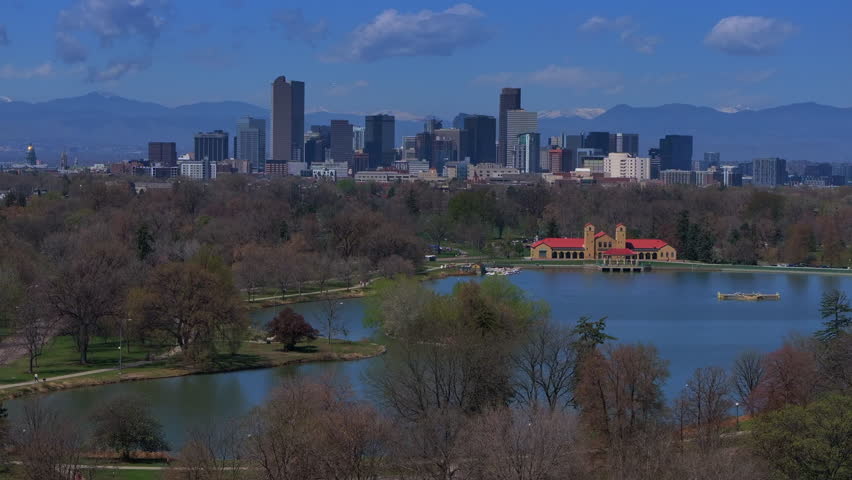 City Park Denver Colorado Lake Pavilion vibrant blossom spring summer aerial drone sunny blue sky snow capped Rocky Mountains front range cityscape green lush grass trees upwards motion