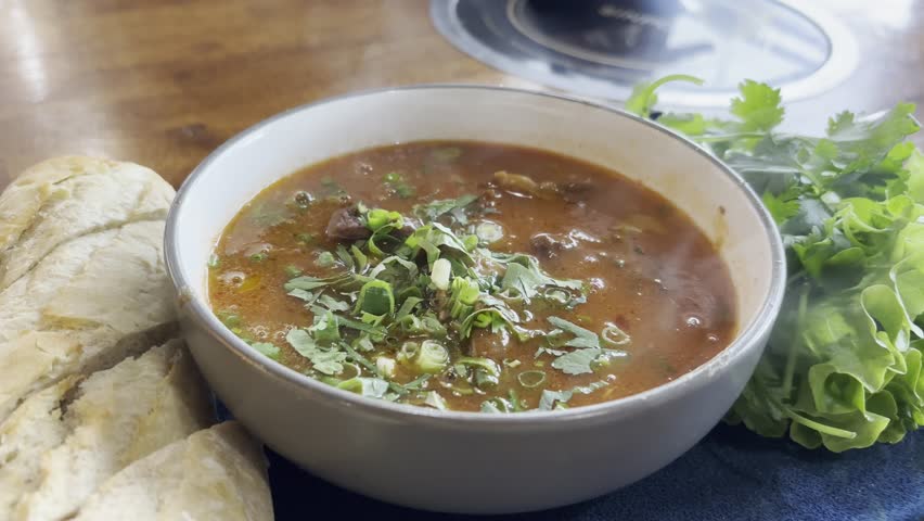A hearty bowl of Vietnamese beef stew, Bo Kho, served with a fresh baguette and herbs. This aromatic dish showcases a rich, flavorful broth perfect for culinary and food blog photography